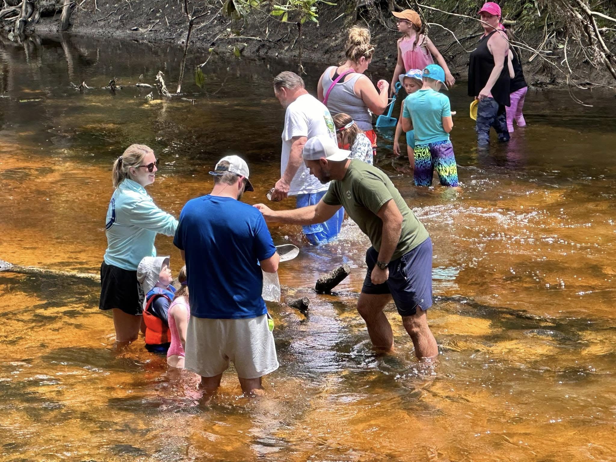 A young boy smiling in the Alafia River with dozens of fossil hunters visible in the background